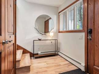 Step into this inviting entryway featuring warm wooden doors and stairs, complemented by a stylish console table with a unique antler-adorned mirror.