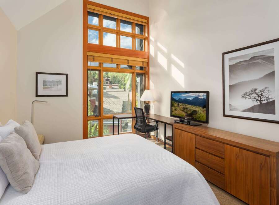 Experience modern comfort in this inviting bedroom, featuring a plush white quilted bed and a large, multi-pane window offering scenic views.