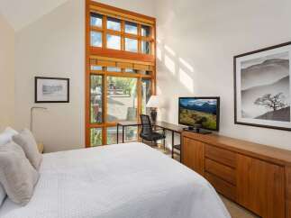 Experience modern comfort in this inviting bedroom, featuring a plush white quilted bed and a large, multi-pane window offering scenic views.