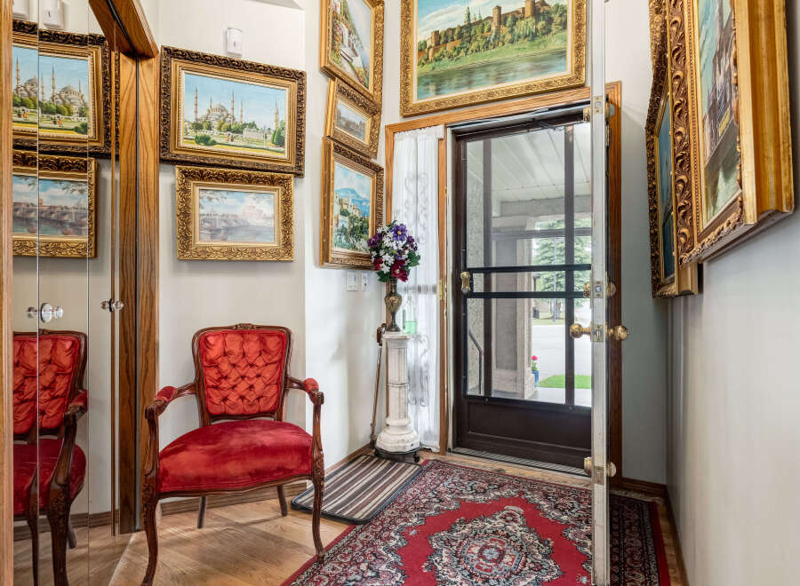 Step into this charming entryway featuring a plush red velvet armchair and a collection of ornate framed landscape paintings.