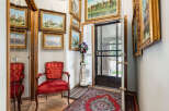 Step into this charming entryway featuring a plush red velvet armchair and a collection of ornate framed landscape paintings.