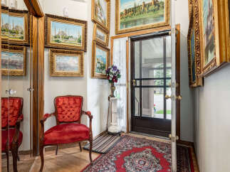 Step into this charming entryway featuring a plush red velvet armchair and a collection of ornate framed landscape paintings.