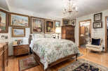 This beautifully decorated bedroom features a luxurious floral comforter on a wooden bed frame, complemented by an ornate chandelier and a collection of framed artwork adorning the walls.