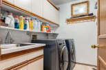 This laundry room features a convenient sink and ample storage with overhead cabinets and open shelving stocked with cleaning supplies.