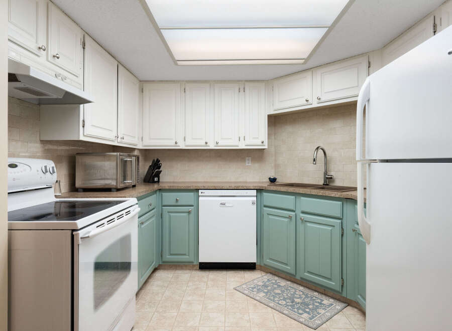 This charming kitchen features white upper cabinets and light teal lower cabinets, offering a bright and airy feel.