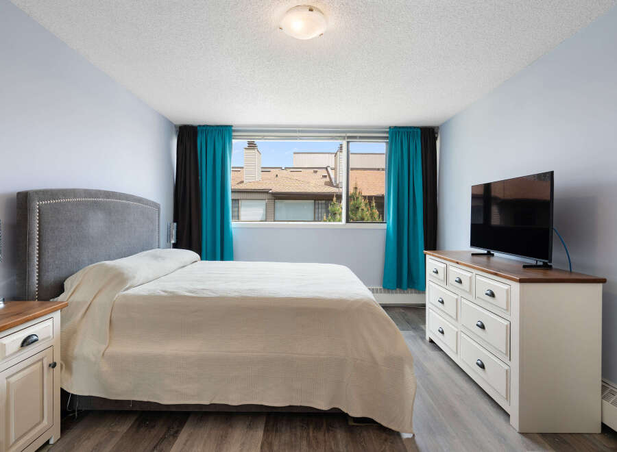 Discover comfort and style in this inviting bedroom, featuring a plush grey upholstered headboard and a cozy, neutral-toned bedspread.