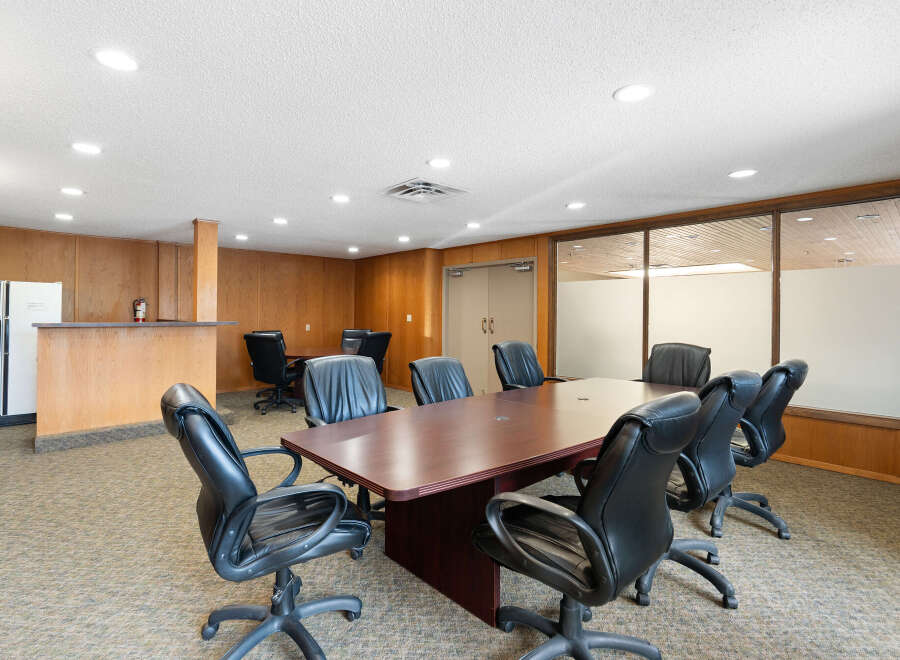 This spacious conference room features a large, polished wood table surrounded by comfortable black leather executive chairs, perfect for productive meetings.