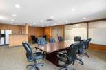 This spacious conference room features a large, polished wood table surrounded by comfortable black leather executive chairs, perfect for productive meetings.