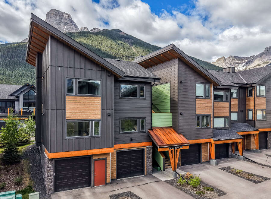 Experience modern mountain living in this stunning townhouse complex, featuring a striking architectural design with dark siding, warm wood accents, and vibrant green and copper details.