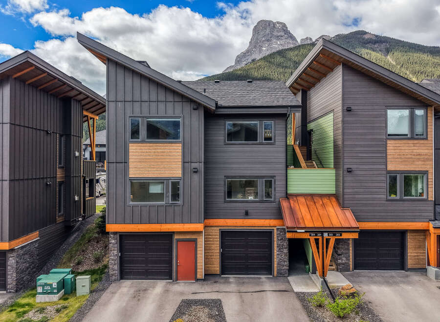 Experience modern mountain living in this stunning townhouse featuring a unique architectural design with a striking angled roofline and a mix of dark metal siding and warm wood accents.