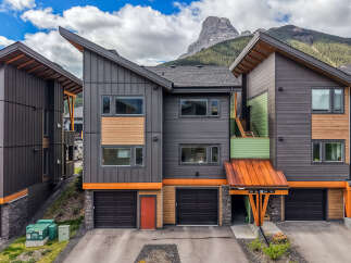 Experience modern mountain living in this stunning townhouse featuring a unique architectural design with a striking angled roofline and a mix of dark metal siding and warm wood accents.