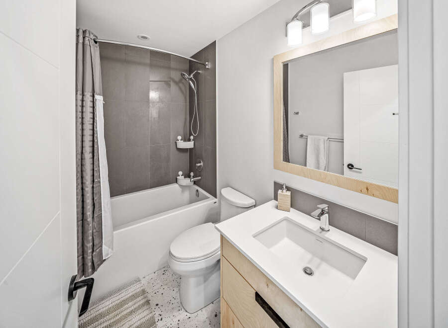 This modern bathroom features a sleek white bathtub with a grey tiled backsplash and a stylish shower curtain.
