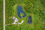 Discover this stunning aerial view of a private estate featuring two serene ponds, a charming golf putting green, and a picturesque island accessible by a wooden bridge.