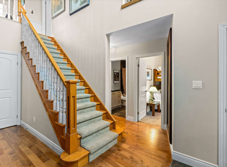 Step into this inviting entryway featuring a grand wooden staircase with plush carpeting and elegant white balusters.