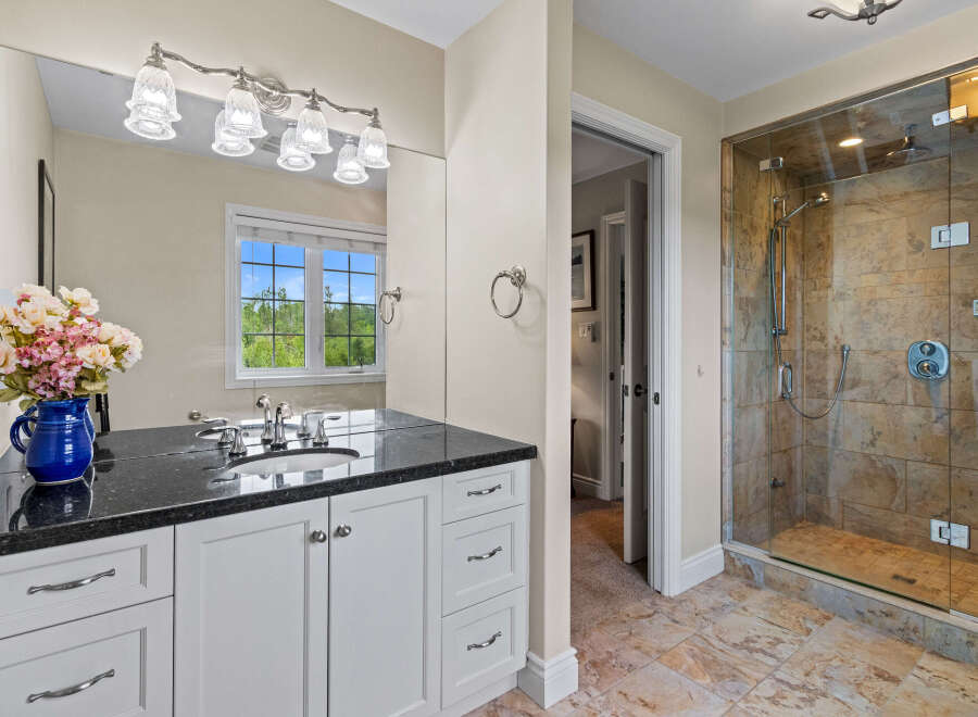 This elegant bathroom features a spacious vanity with a granite countertop and ample storage, complemented by a large mirror and decorative lighting.
