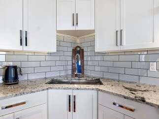 This modern kitchen features sleek white cabinetry and a stunning granite countertop, perfect for meal preparation.