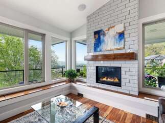 Experience breathtaking panoramic views from this stunning living room, featuring a modern gas fireplace with a white subway tile surround and a rustic wooden mantel.