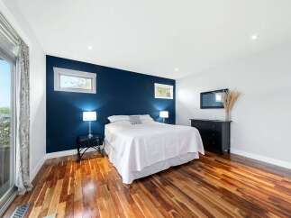 Experience modern comfort in this stunning bedroom, featuring a striking navy accent wall that beautifully complements the rich hardwood floors.