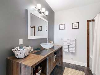 This rustic bathroom features a unique wooden vanity with a vessel sink, complemented by a large framed mirror and a modern light fixture.