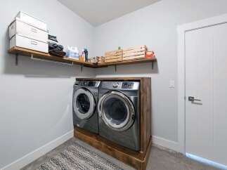 This laundry room features a modern Samsung washer and dryer set, elegantly housed on a custom wooden platform.