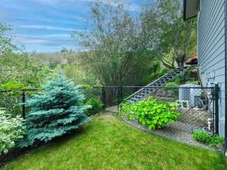 Discover this charming backyard oasis featuring a lush green lawn, a mature blue spruce tree, and vibrant landscaping.