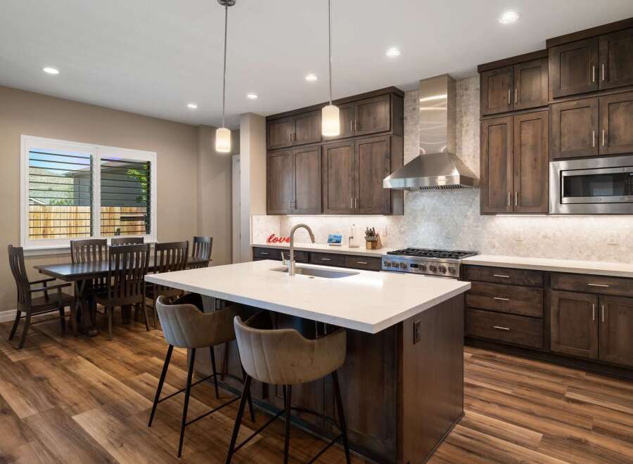 Experience modern luxury in this stunning kitchen, featuring rich dark wood cabinetry, a sleek stainless steel range hood, and a spacious quartz island perfect for entertaining.