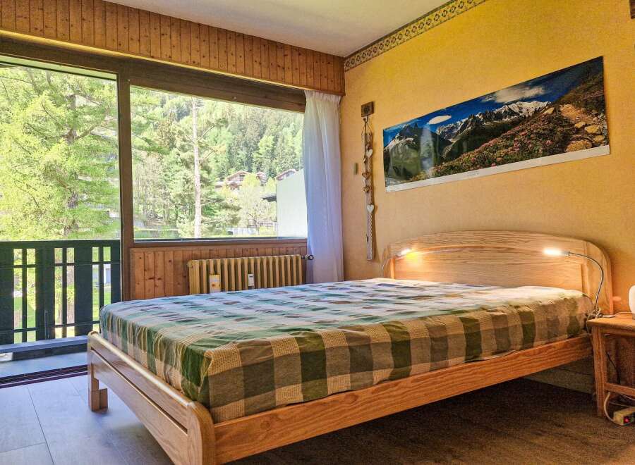 Experience serene mountain living in this charming bedroom, featuring a comfortable wooden bed adorned with a classic plaid comforter.