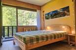 Experience serene mountain living in this charming bedroom, featuring a comfortable wooden bed adorned with a classic plaid comforter.