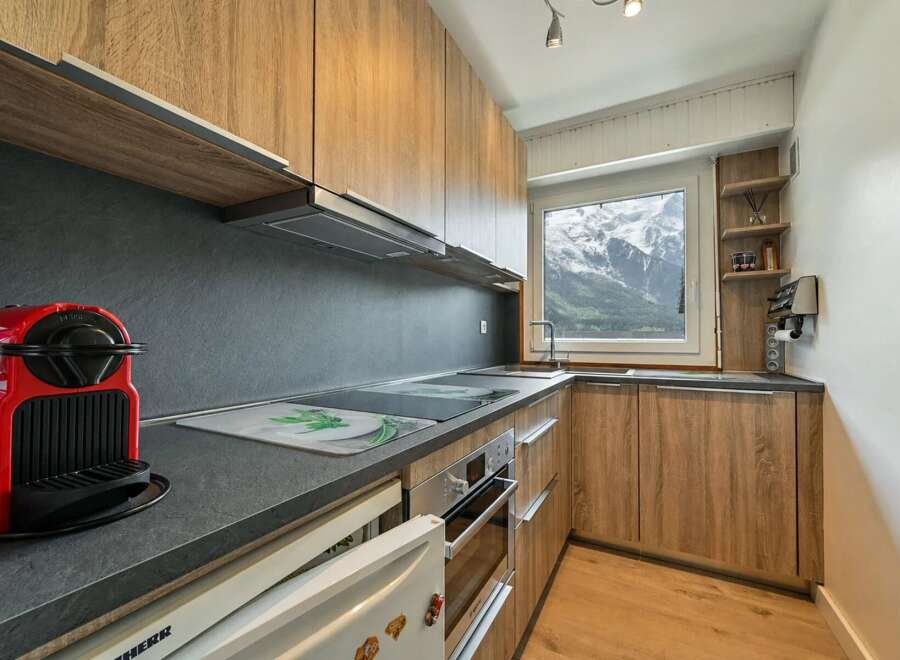 Experience breathtaking mountain views from this modern kitchen, featuring sleek wooden cabinetry and a dark stone countertop.