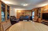 This inviting living room features a warm, wood-paneled ambiance, complemented by comfortable leather sofas and a large, light-wood dining table perfect for gatherings.