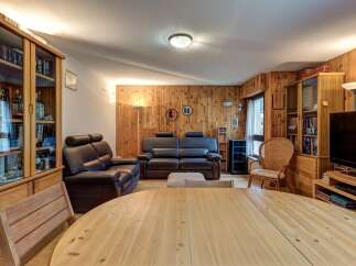 This inviting living room features a warm, wood-paneled ambiance, complemented by comfortable leather sofas and a large, light-wood dining table perfect for gatherings.