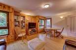 Experience cozy living in this charming wood-paneled living room, featuring a comfortable seating area with a plush ottoman and a dedicated dining space with a round wooden table and chairs.