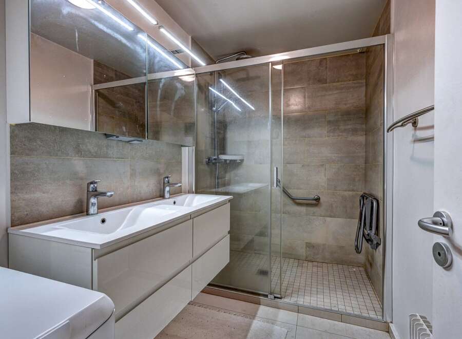 This modern bathroom features a spacious double vanity with sleek chrome fixtures, complemented by a large mirrored cabinet above.