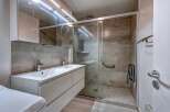 This modern bathroom features a spacious double vanity with sleek chrome fixtures, complemented by a large mirrored cabinet above.