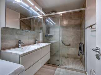 This modern bathroom features a spacious double vanity with sleek chrome fixtures, complemented by a large mirrored cabinet above.