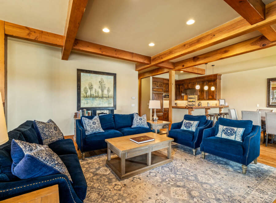 Experience rustic elegance in this spacious living area, featuring exposed wooden beams and a cozy seating arrangement centered around a coffee table.