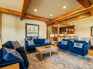 Experience rustic elegance in this spacious living area, featuring exposed wooden beams and a cozy seating arrangement centered around a coffee table.