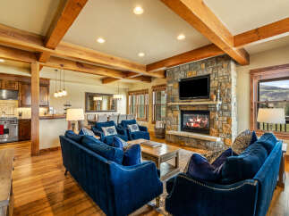 Experience luxurious mountain living in this stunning great room, featuring a grand stone fireplace and exposed wooden beams that add rustic charm.