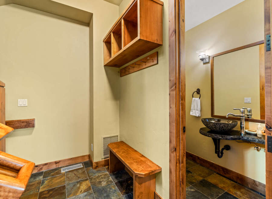 This rustic entryway features a wooden bench and a wall-mounted shelf with hooks, perfect for storing coats and accessories.