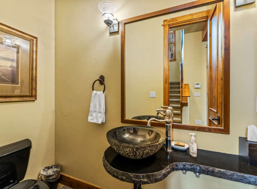 This powder room features a unique stone vessel sink atop a live-edge granite vanity, complemented by a polished chrome faucet.