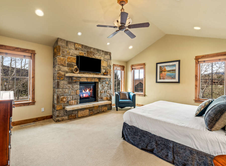 Experience ultimate comfort in this luxurious bedroom, featuring a stunning stone fireplace with a mounted television for cozy evenings.