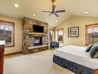 Experience ultimate comfort in this luxurious bedroom, featuring a stunning stone fireplace with a mounted television for cozy evenings.