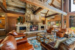 Experience rustic luxury in this stunning living room featuring a grand stone fireplace with a crackling fire, complemented by exposed wooden beams and a vaulted ceiling.