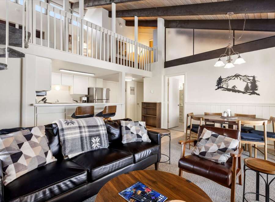 Experience modern living in this stunning loft-style condo, featuring a sleek black leather sofa and a cozy armchair perfect for relaxation.