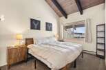 Experience cozy mountain living in this charming bedroom featuring a vaulted wood-beamed ceiling and a large window offering scenic views.