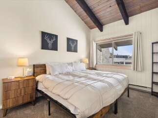 Experience cozy mountain living in this charming bedroom featuring a vaulted wood-beamed ceiling and a large window offering scenic views.