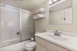 This bright and clean bathroom features a spacious bathtub with a sliding glass shower door and white tiled walls.