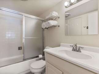 This bright and clean bathroom features a spacious bathtub with a sliding glass shower door and white tiled walls.