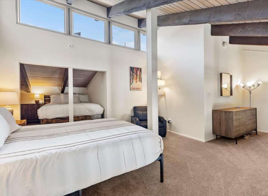 Experience ultimate comfort in this spacious bedroom featuring a vaulted ceiling with exposed beams and large windows that flood the room with natural light.