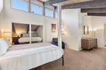 Experience ultimate comfort in this spacious bedroom featuring a vaulted ceiling with exposed beams and large windows that flood the room with natural light.